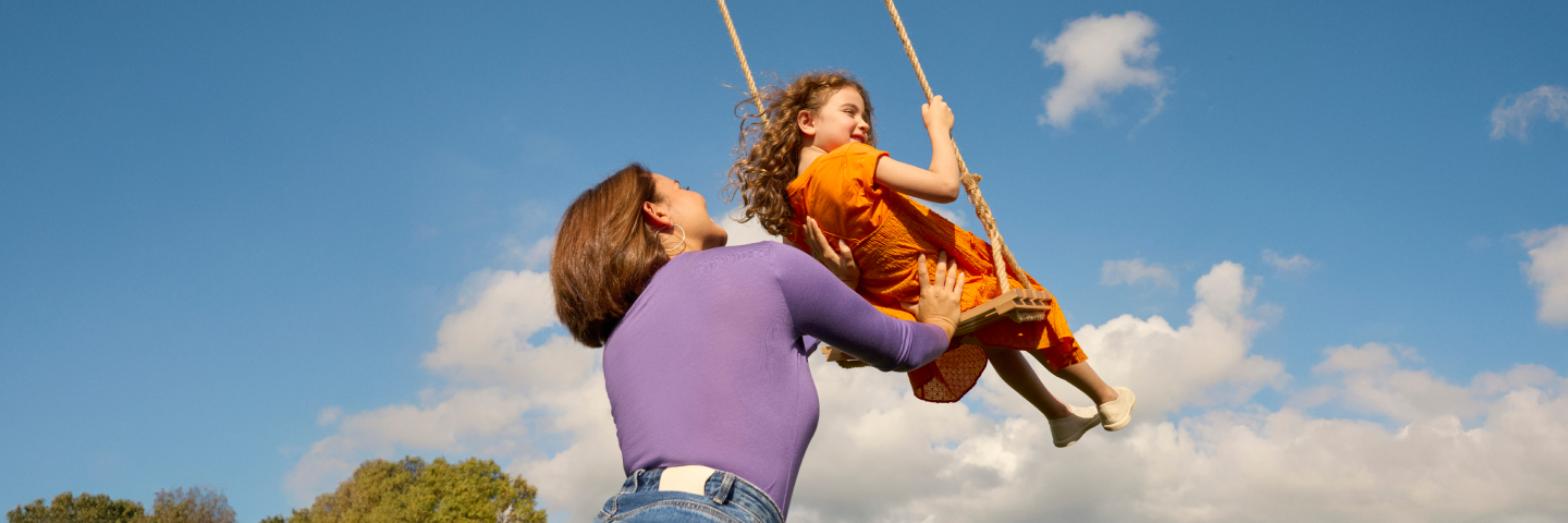 A happy girl swings high on a rope swing as her mother looks on, enjoying an allergy free sunny day outdoors.